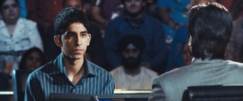 Movie still from “Slumdog Millionaire” (2008), directed by Danny Boyle – A man sitting in front of a group of people; Close Up shot, Over the shoulder angle