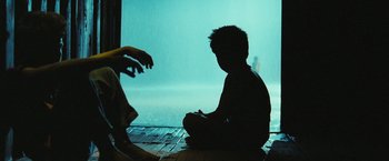 Movie still from “Slumdog Millionaire” (2008), directed by Danny Boyle – A child sitting on the ground in front of a person; Wide shot, Over the shoulder angle