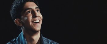 Movie still from “Slumdog Millionaire” (2008), directed by Danny Boyle – A young man smiles brightly as he looks upward; Close Up shot, Low angle