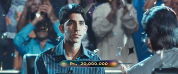 Movie still from “Slumdog Millionaire” (2008), directed by Danny Boyle – A man in a crowd of onlookers in front of an audience; Close Up shot, High angle