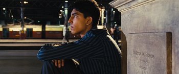 Movie still from “Slumdog Millionaire” (2008), directed by Danny Boyle – A man sitting on top of a bench at night; Medium shot, Low angle