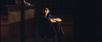 Movie still from “Slumdog Millionaire” (2008), directed by Danny Boyle – A man sitting on a chair in a dark room; Medium shot, High angle