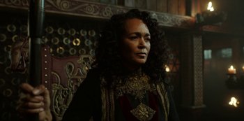 Movie still from “Vikings: Valhalla” (2022), created by Jeb Stuart – A woman with long curly black hair wearing a black and gold dress; Close Up shot, Over the shoulder angle