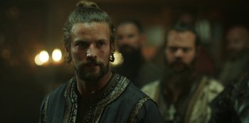 Movie still from “Vikings: Valhalla” (2022), created by Jeb Stuart – A man with long hair and beard standing next to other men; Close Up shot, Over the shoulder angle