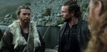 Movie still from “Vikings: Valhalla” (2022), created by Jeb Stuart – Two bearded men standing next to a body of water; Medium shot, Over the shoulder angle