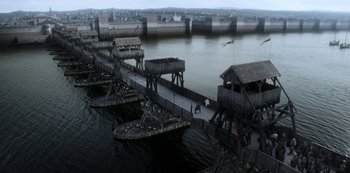 Movie still from “Vikings: Valhalla” (2022), created by Jeb Stuart – An aerial view of a pier with a bridge and buildings in the background; Extreme Wide shot, High angle