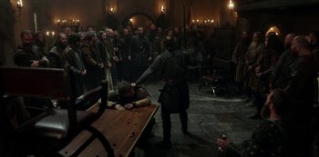 Movie still from “Vikings: Valhalla” (2022), created by Jeb Stuart – A man in medieval garb standing next to a table; Wide shot, High angle
