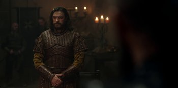 Movie still from “Vikings: Valhalla” (2022), created by Jeb Stuart – A man in a brown and gold outfit stands in front of candles; Medium shot, Over the shoulder angle