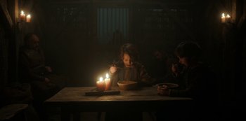 Movie still from “Vikings: Valhalla” (2022), created by Jeb Stuart – A little girl sitting at a table with a bowl of noodles and candles; Medium shot, Low angle