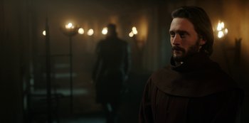 Movie still from “Vikings: Valhalla” (2022), created by Jeb Stuart – A man standing in a dark room with lights in the background; Medium shot, Over the shoulder angle