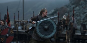 Movie still from “Vikings: Valhalla” (2022), created by Jeb Stuart – A woman is holding a sword and a shield; Medium shot, Low angle