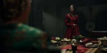 Movie still from “Vikings: Valhalla” (2022), created by Jeb Stuart – A woman standing in front of a table with food on top of it; Medium shot, Over the shoulder angle