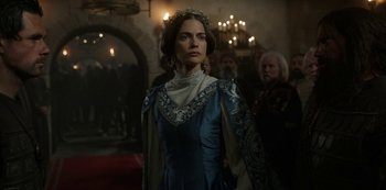 Movie still from “Vikings: Valhalla” (2022), created by Jeb Stuart – A woman in a blue dress standing in front of a group of people; Medium shot, Over the shoulder angle