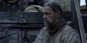 Movie still from “Vikings: Valhalla” (2022), created by Jeb Stuart – A man with long grey hair and a beard sitting on a bench; Close Up shot, Low angle
