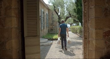 Movie still from “Before Midnight” (2013), directed by Richard Linklater – A man walking down a street holding two bags; Wide shot, Low angle