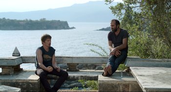 Movie still from “Before Midnight” (2013), directed by Richard Linklater – Two men sitting on a bench near a body of water; Medium shot, Over the shoulder angle