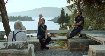 Movie still from “Before Midnight” (2013), directed by Richard Linklater – Two men sitting on a stone bench near a body of water; Wide shot, Over the shoulder angle