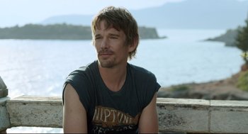 Movie still from “Before Midnight” (2013), directed by Richard Linklater – A person sitting on a ledge near a body of water; Close Up shot, Over the shoulder angle