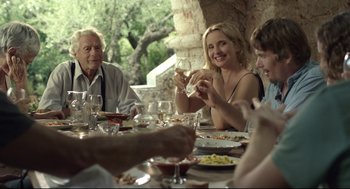 Movie still from “Before Midnight” (2013), directed by Richard Linklater – A group of people sitting at a table with plates of food; Medium shot, Over the shoulder angle