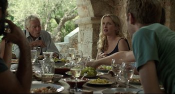 Movie still from “Before Midnight” (2013), directed by Richard Linklater – A group of people sitting at a table with plates of food on it; Medium shot, Over the shoulder angle