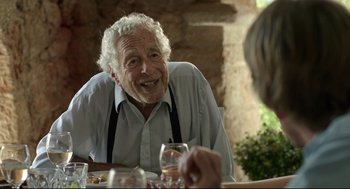 Movie still from “Before Midnight” (2013), directed by Richard Linklater – An older man sitting at a table with a glass of wine; Close Up shot, Over the shoulder angle