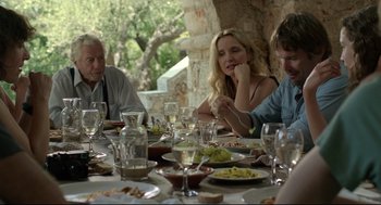 Movie still from “Before Midnight” (2013), directed by Richard Linklater – A group of people sitting at a table with plates of food on it; Medium shot, Over the shoulder angle