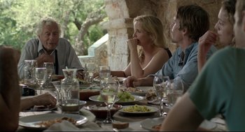 Movie still from “Before Midnight” (2013), directed by Richard Linklater – A group of people sitting at a table with plates of food on it; Medium shot, Over the shoulder angle