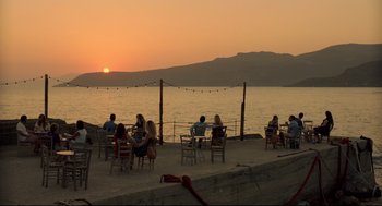 Movie still from “Before Midnight” (2013), directed by Richard Linklater – A group of people sitting at tables on the beach at sunset; Extreme Wide shot, High angle
