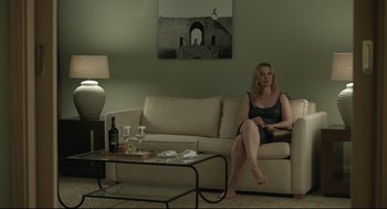 Movie still from “Before Midnight” (2013), directed by Richard Linklater – A woman sitting on top of a couch in a living room; Wide shot, Over the shoulder angle