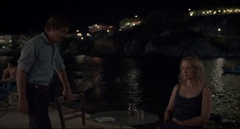 Movie still from “Before Midnight” (2013), directed by Richard Linklater – A man and a woman sitting at a table by a body of water at night; Medium shot, Over the shoulder angle