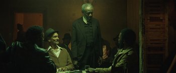 Movie still from “Small Axe” (2020), directed by Steve McQueen – A group of people sitting around a table; Medium shot, Over the shoulder angle