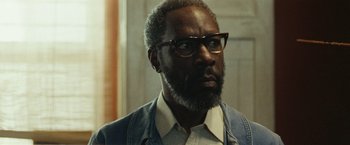 Movie still from “Small Axe” (2020), directed by Steve McQueen – A person wearing glasses and a jacket; Close Up shot, Low angle