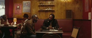 Movie still from “Small Axe” (2020), directed by Steve McQueen – Two men are sitting at a table in a restaurant; Medium shot, Over the shoulder angle