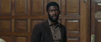 Movie still from “Small Axe” (2020), directed by Steve McQueen – A man in a brown jacket and a brown shirt; Medium shot, High angle