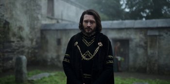 Movie still from “Vikings: Valhalla” (2022), created by Jeb Stuart – A man in a black outfit standing in front of a building; Medium shot, Over the shoulder angle