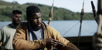 Movie still from “Vikings: Valhalla” (2022), created by Jeb Stuart – A man holding a fishing rod while standing on a boat; Medium shot, Over the shoulder angle