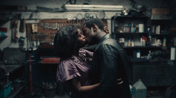 Movie still from “Small Axe” (2020), directed by Steve McQueen – A man and a woman kissing in a garage; Medium shot, High angle