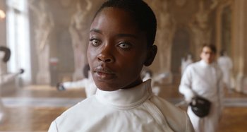 Movie still from “Wednesday” (2022), created by Miles Millar – A woman wearing a white shirt and standing in front of a statue; Close Up shot, Over the shoulder angle