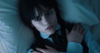 Movie still from “Wednesday” (2022), created by Miles Millar – A woman in a suit and tie laying in a bed; Close Up shot, Low angle