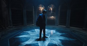 Movie still from “Wednesday” (2022), created by Miles Millar – A person standing in a room with a blue light; Wide shot, High angle