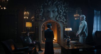 Movie still from “Wednesday” (2022), created by Miles Millar – A woman standing in front of a fire place; Wide shot, Over the shoulder angle