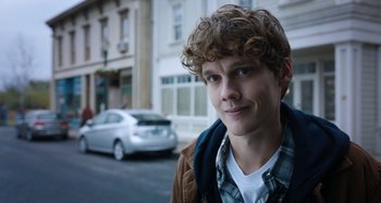 Movie still from “Wednesday” (2022), created by Miles Millar – A young man standing on the side of the street; Close Up shot, Over the shoulder angle