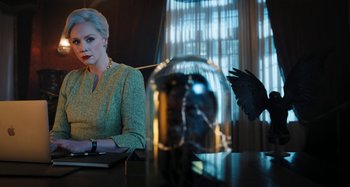 Movie still from “Wednesday” (2022), created by Miles Millar – A woman sitting in front of a computer on top of a table; Medium shot, Low angle