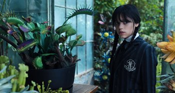 Movie still from “Wednesday” (2022), created by Miles Millar – A girl standing in front of a potted plant; Medium shot, Over the shoulder angle