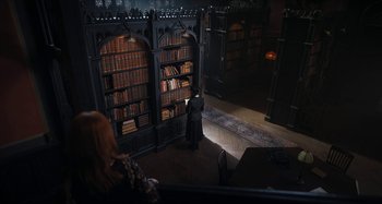 Movie still from “Wednesday” (2022), created by Miles Millar – A person standing in front of a book shelf; Extreme Wide shot, High angle