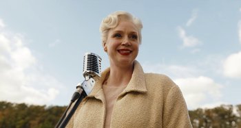 Movie still from “Wednesday” (2022), created by Miles Millar – An older woman holding an old fashioned microphone; Close Up shot, Low angle