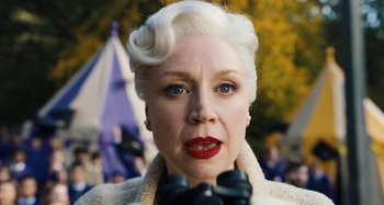 Movie still from “Wednesday” (2022), created by Miles Millar – An older woman wearing a white coat and red lipstick; Close Up shot, Low angle