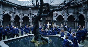Movie still from “Wednesday” (2022), created by Miles Millar – A group of people sitting around a pond with a tree in the middle of it; Wide shot, High angle