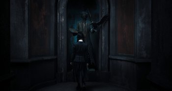 Movie still from “Wednesday” (2022), created by Miles Millar – A man and a woman are standing in front of a statue; Wide shot, Low angle