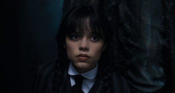 Movie still from “Wednesday” (2022), created by Miles Millar – A young woman with long black hair wearing a suit and tie; Close Up shot, High angle